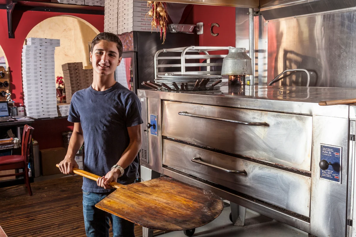 Teenage boy holding spatula in pizza restaurant