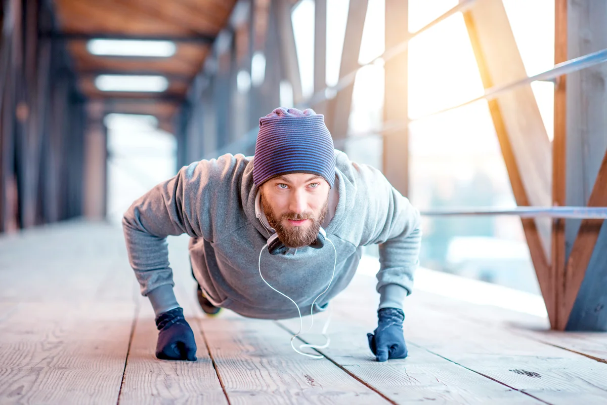 Man in hat and sweatshirt doing pushing-ups outdoors