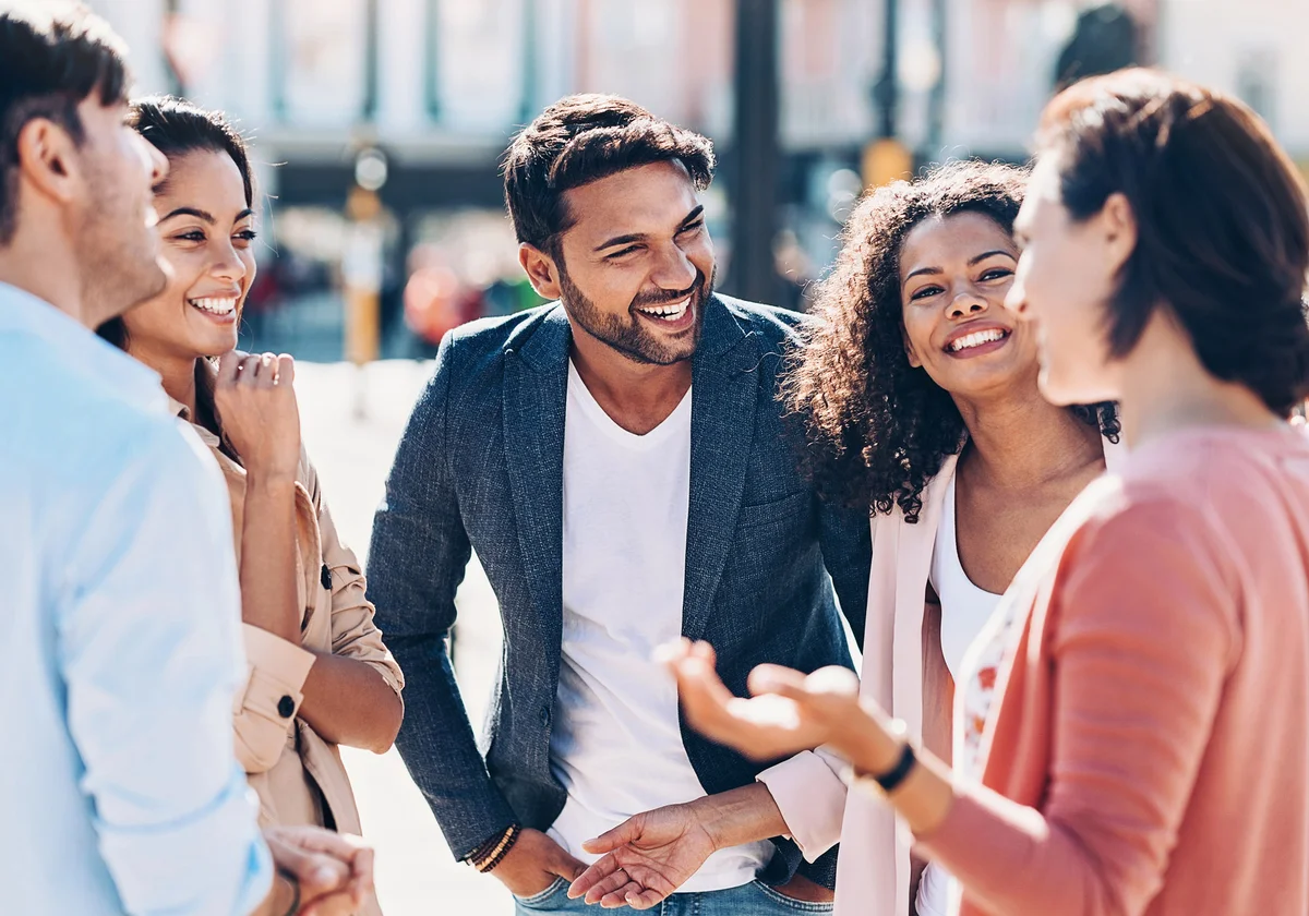 group of smiling young people talking outdoors in the city