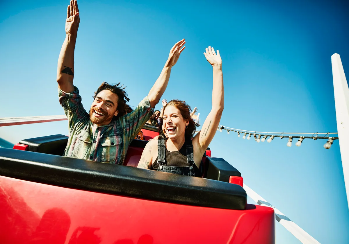 Laughing couple with arms raised riding roller coaster