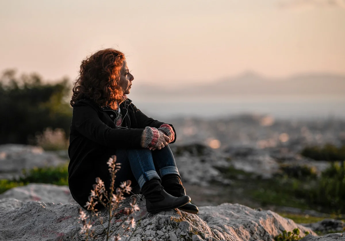 A woman enjoys a sunset sitting on a rocky hill