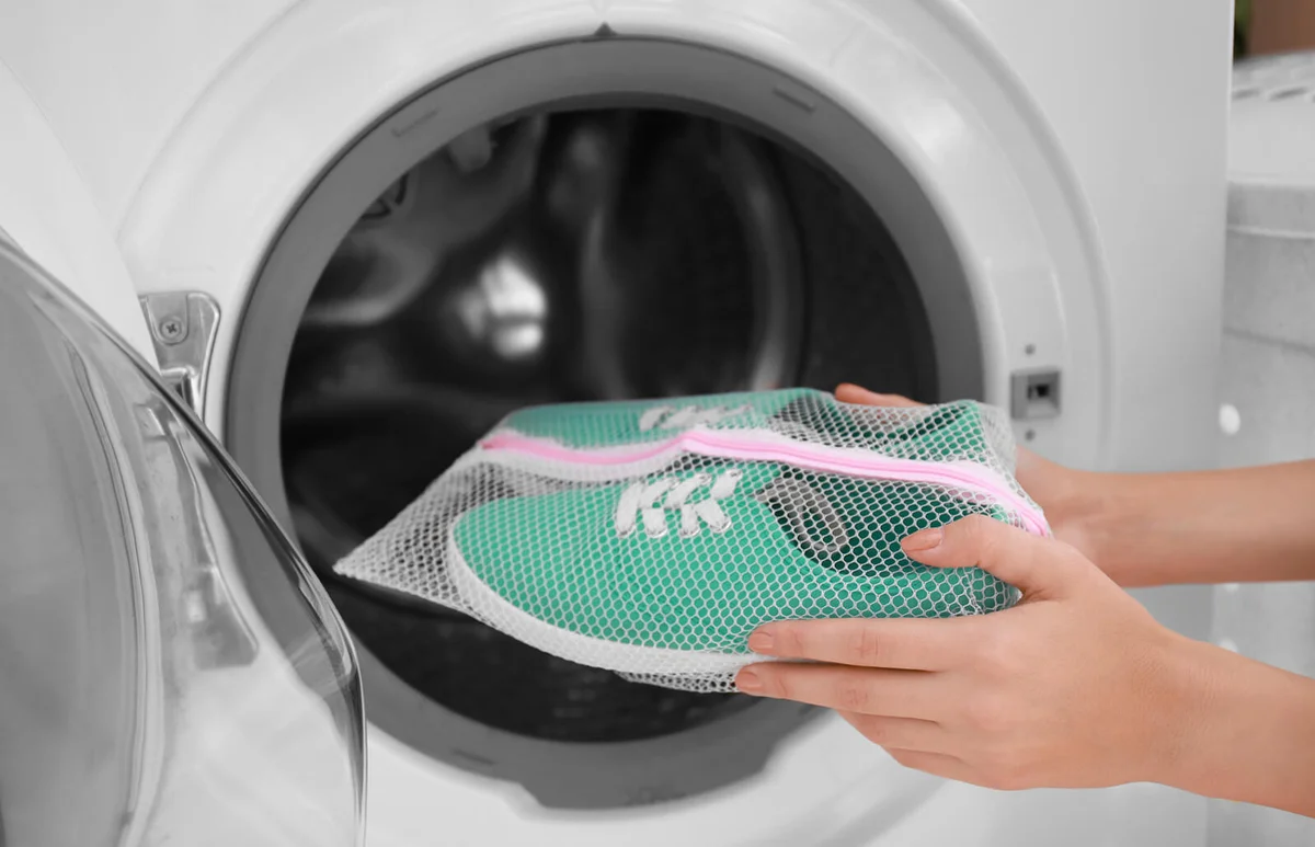 Woman putting mesh with turquoise sneakers into washing machine