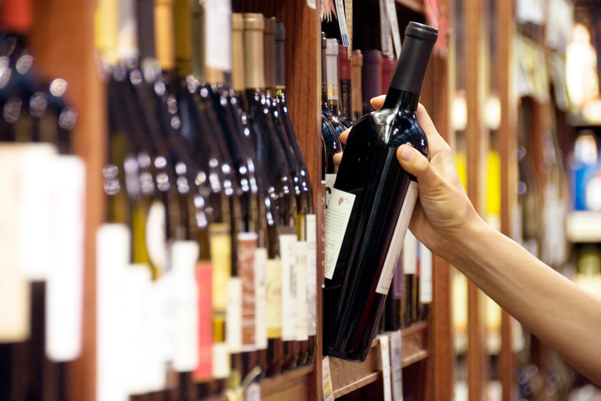 A woman's hand reaches out to select a bottle of red wine
