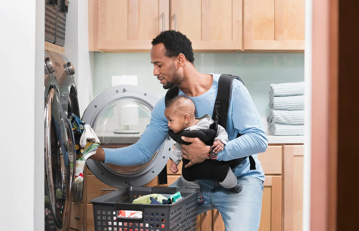 father with son in baby carrier doing laundry