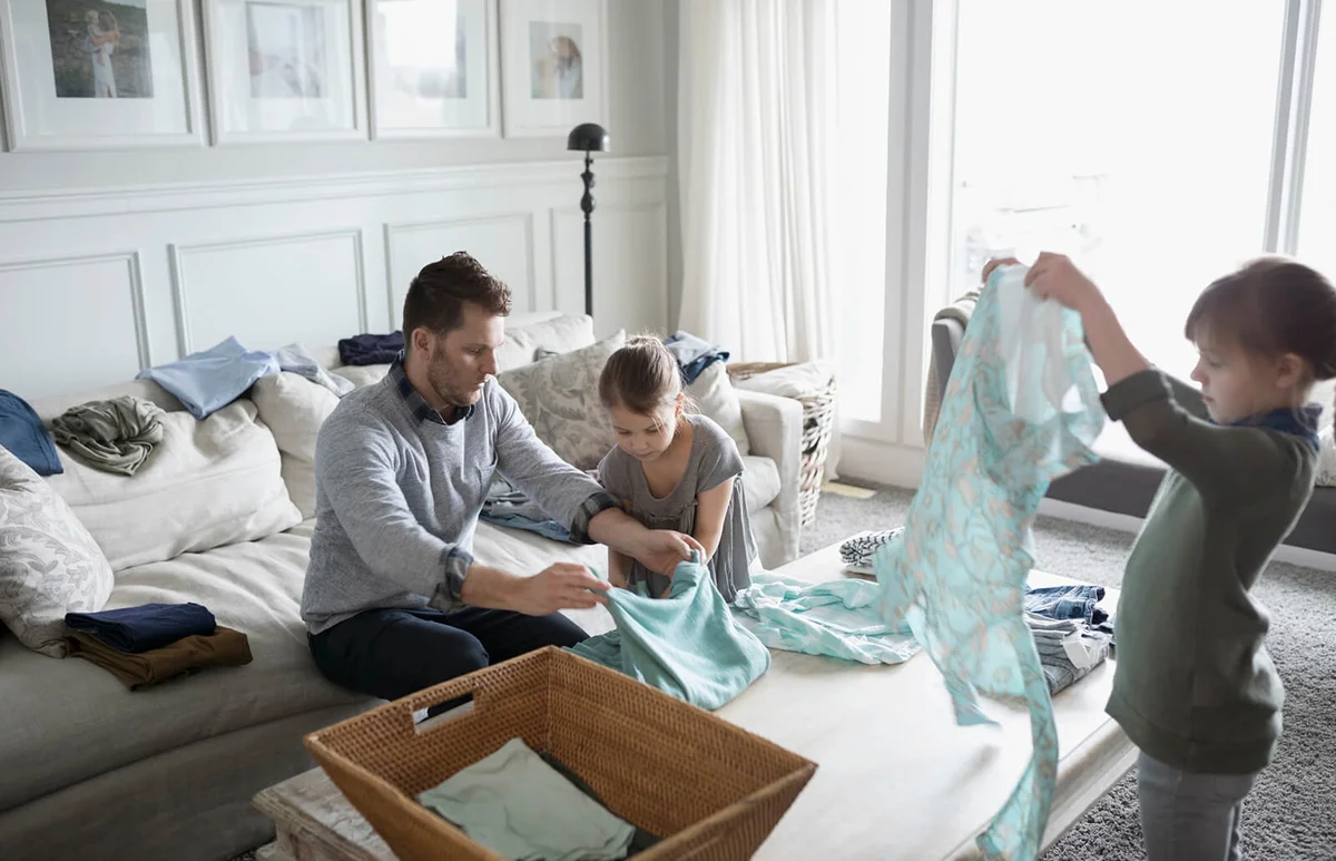 Father and daughters folding laundry in living room