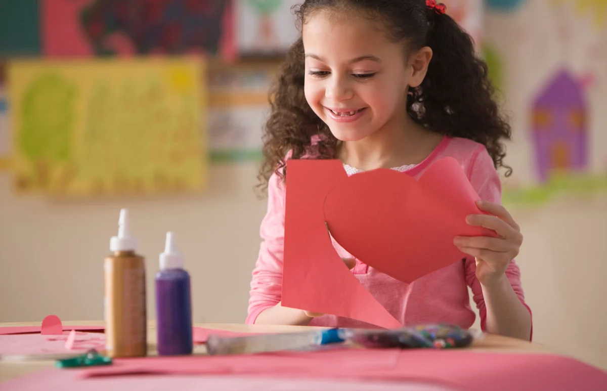 Girl cutting out Valentine's heart in classroom