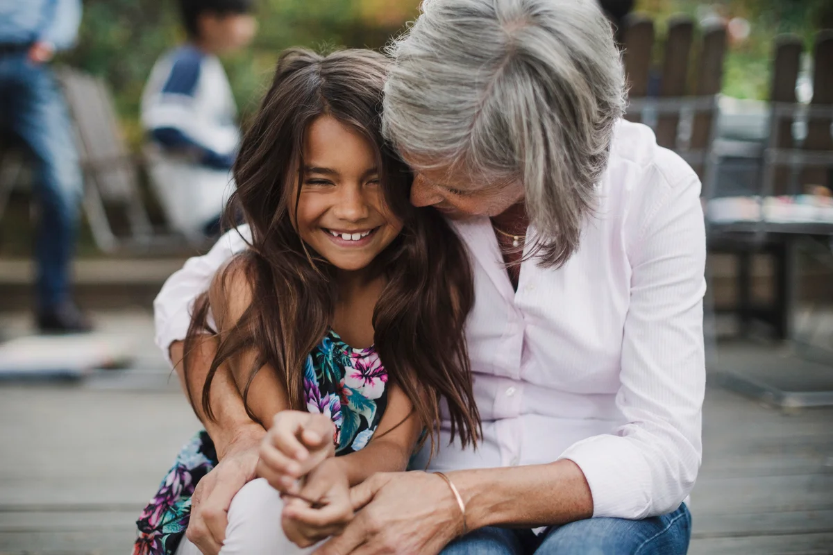 Senior woman embracing granddaughter while sitting at yar