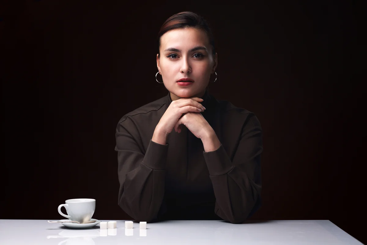 Portrait of a beautiful girl in a classic dress at a glossy table with a white Cup