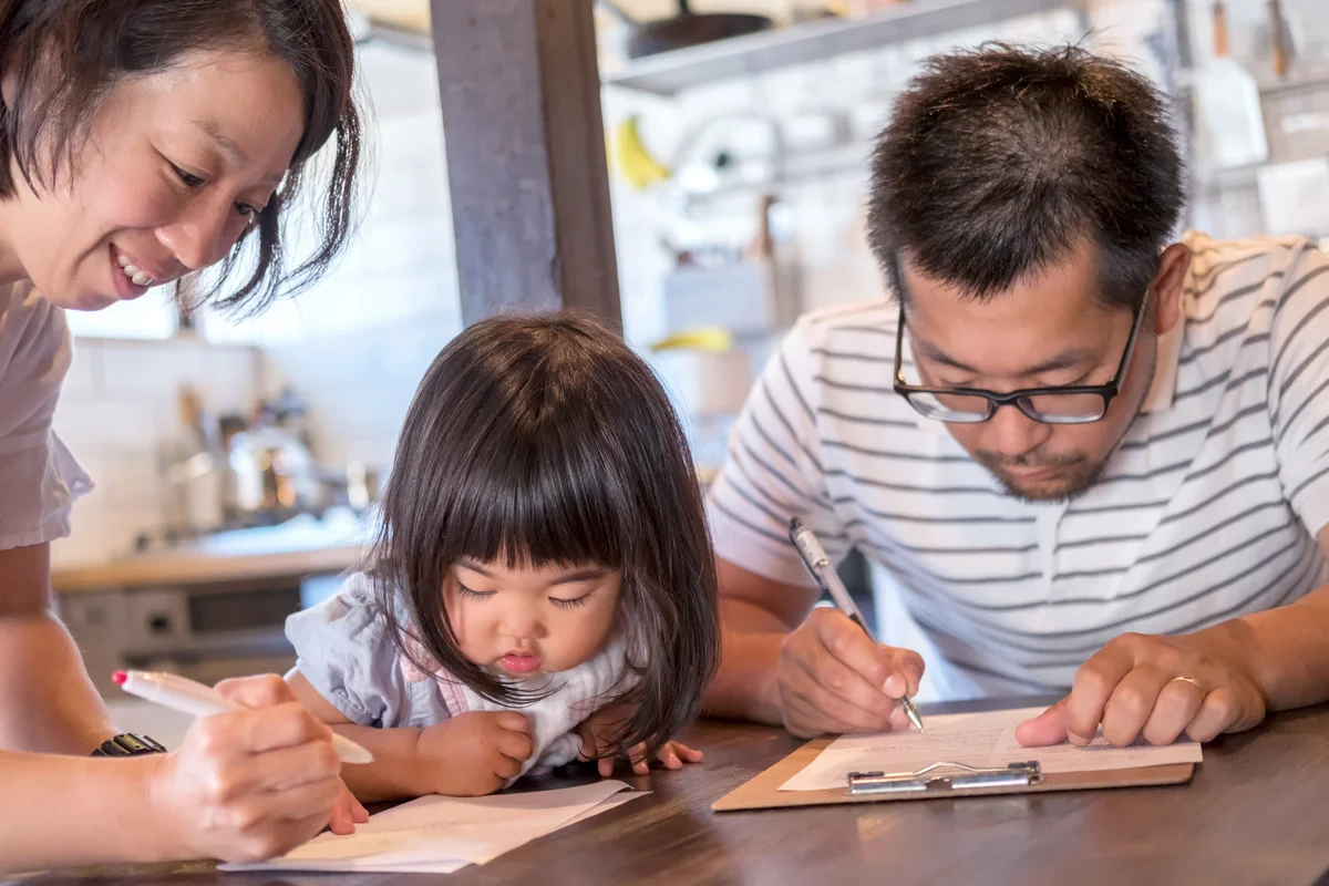 Husband and Wife Fill Out Paperwork While Young Daughter Watches