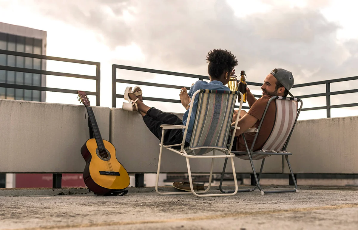Young couple with beer and guitar sitting on rooftop