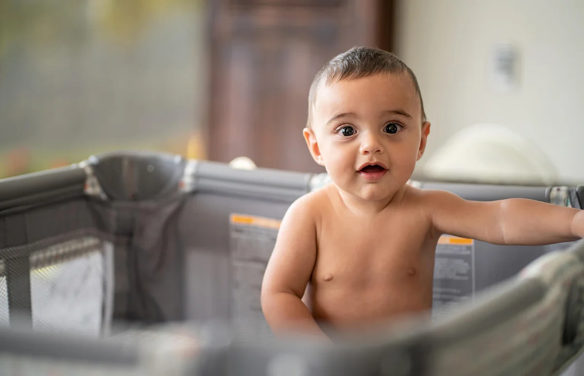 Cute little baby in playpen looking at camera with amazement