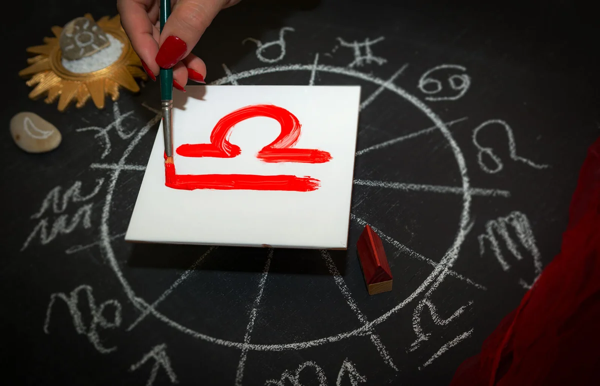 Female astrologer draws libra zodiac sign on white tile
