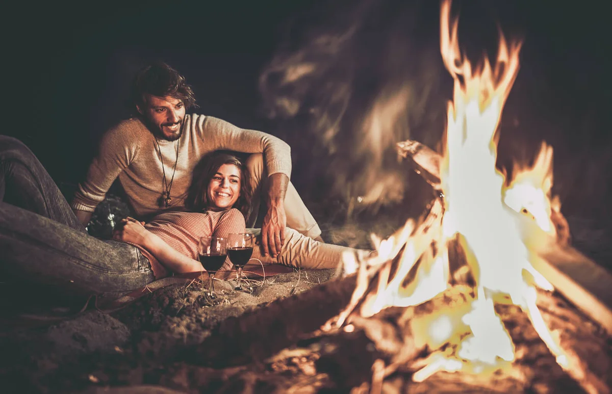 Young happy couple relaxing on the beach by the campfire at night