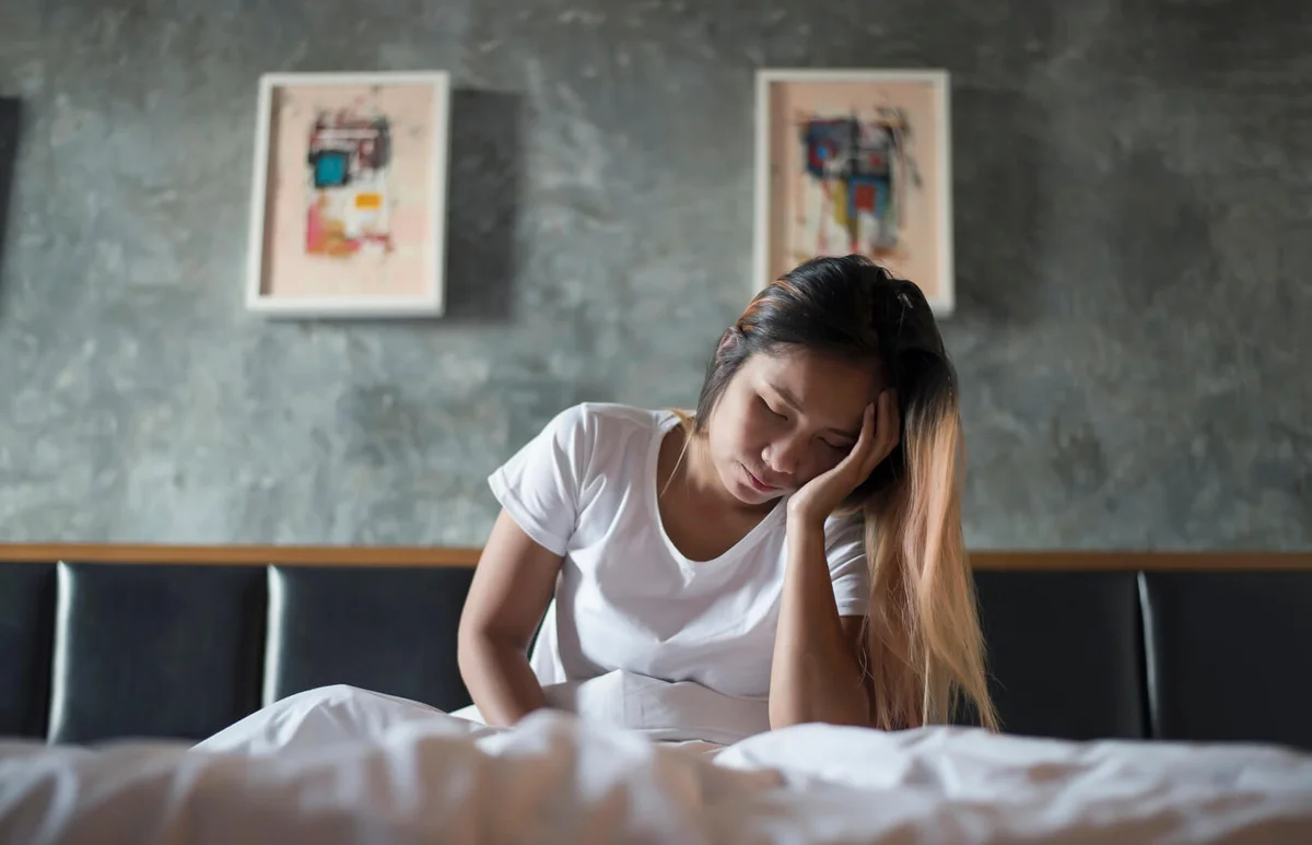Woman With Headache Sitting On Bed At Home