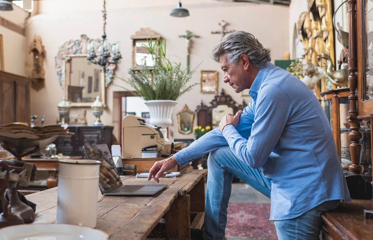 Mature male owner of antique store using laptop in his shop