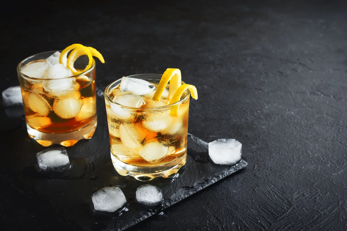 Whiskey on rocks with lemon twist on black stone background