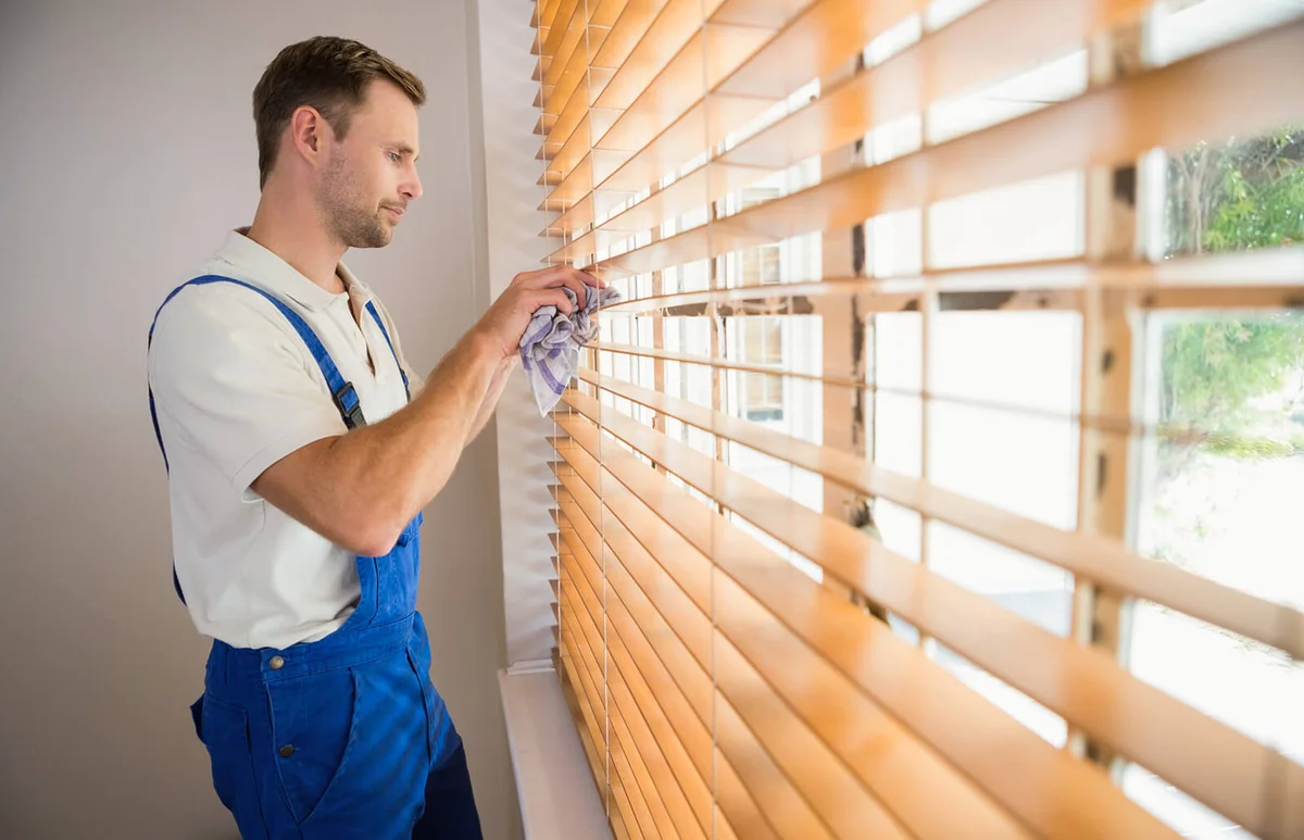 Handyman cleaning blinds with a towel