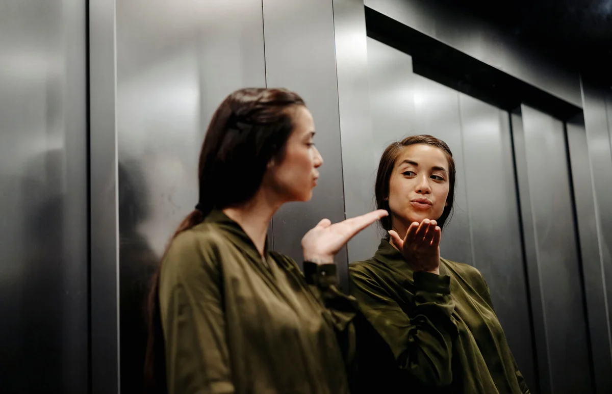 Young woman looking in mirror in elevator blowing a kiss