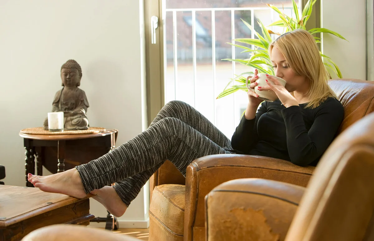 Blond young woman sitting in armchair drinking tea