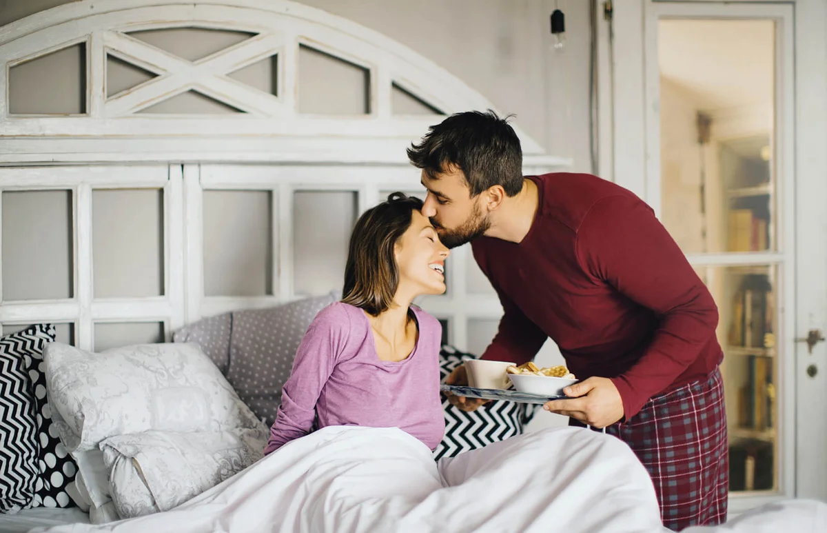 Boyfriend bringing his girlfriend breakfast and kissing her on the forehead