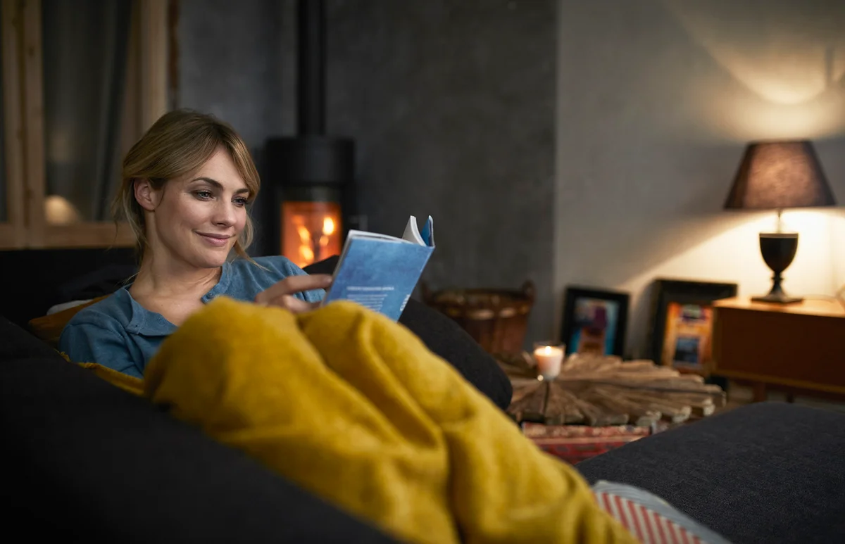 woman reading a book on couch at home in the evening