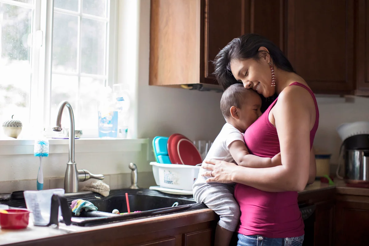 Mom Holds Baby While Leaning In To Kitchen Counter