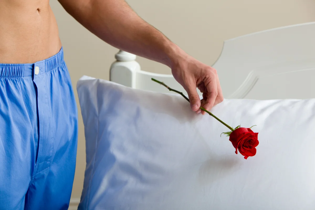 Man leaving single red rose on bed pillow