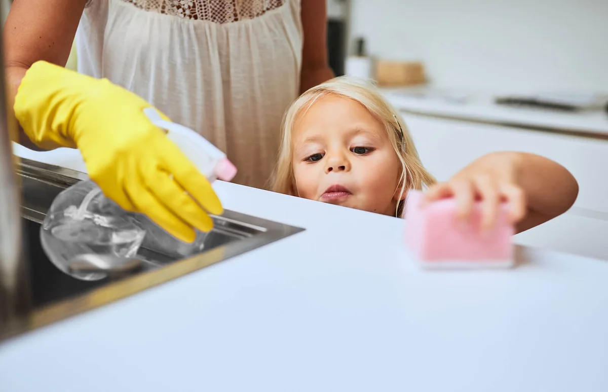 mother and her little daughter cleaning a kitchen surface together at home