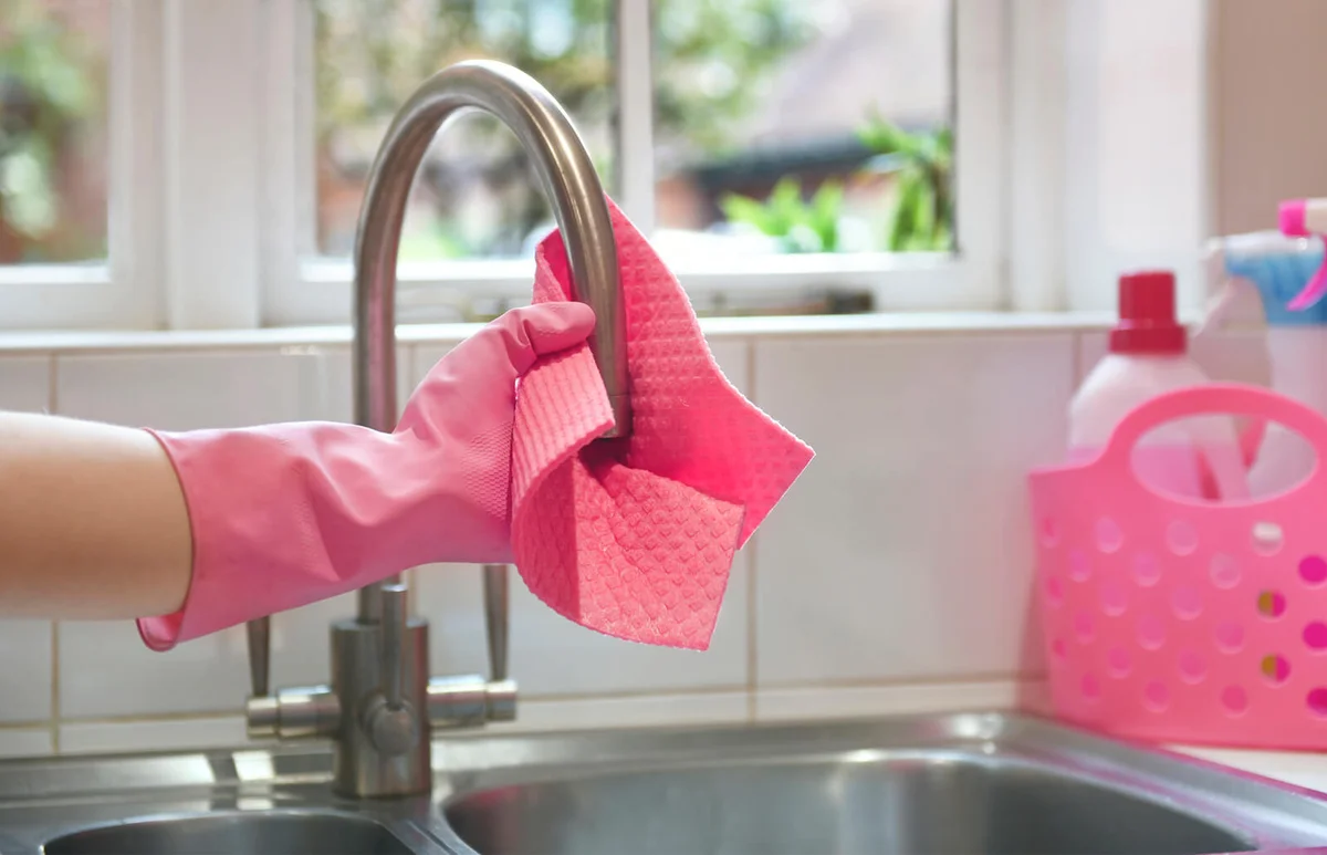 Spring cleaner rinsing cloth under tap in kitchen