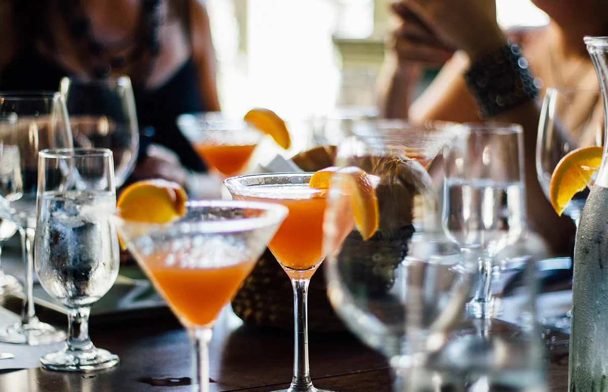 Midsection Of Friends Sitting By Martinis On Table At Restaurant