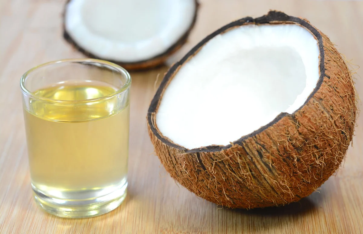 Coconut oil in a glass cup and split coconuts