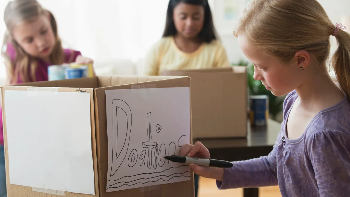 Girl drawing donation sign on cardboard box