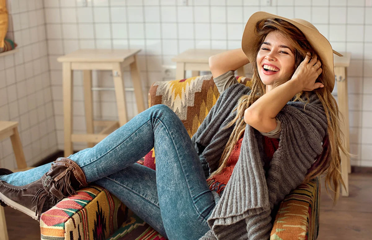 Hippie girl in hat is laughing in cafe chair