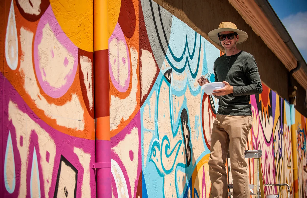 man standing on ladder painting mural on wall