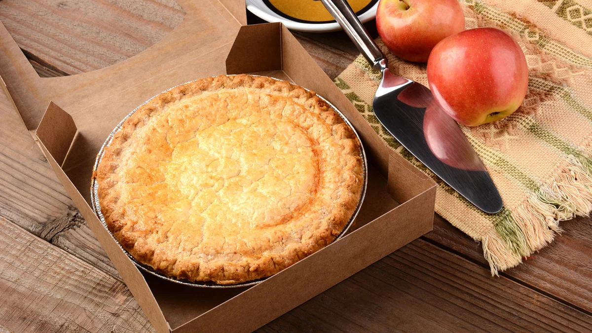 fresh apple pie in a bakery box on a rustic wood table