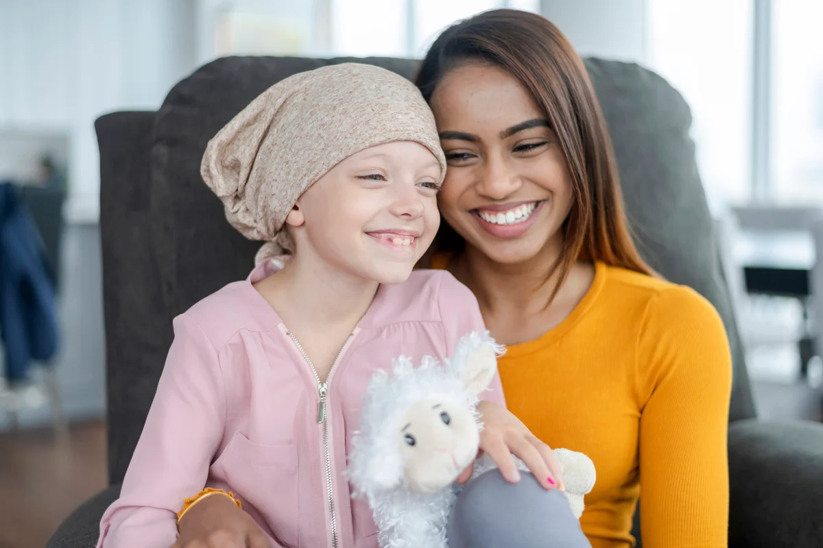 An elementary age girl with cancer sits on her mother's lap