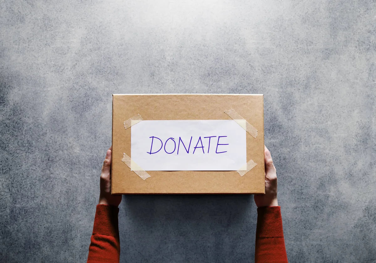 Hands Holding Cardboard Box With Donate Text On Table