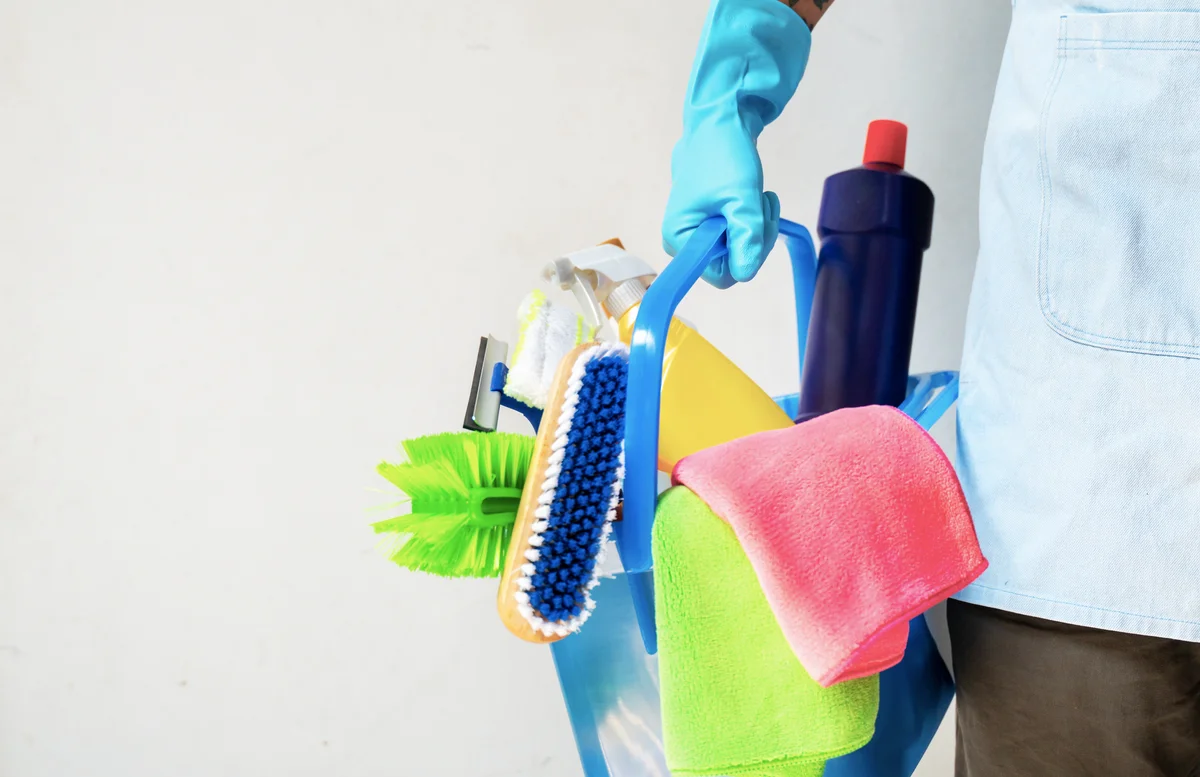 Man holding mop and plastic bucket with brushes, gloves and detergents