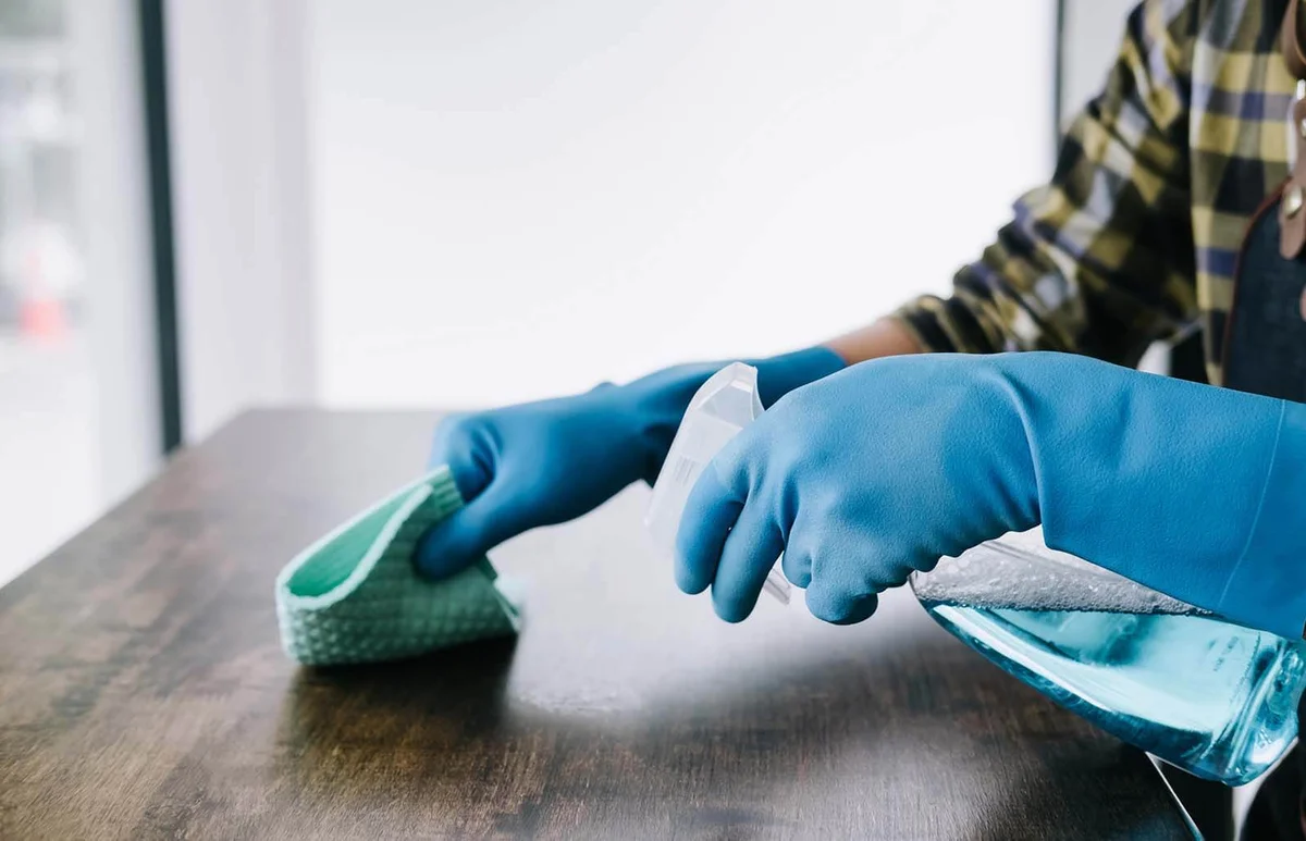 Person Using Disinfectant To Clean Table At Home