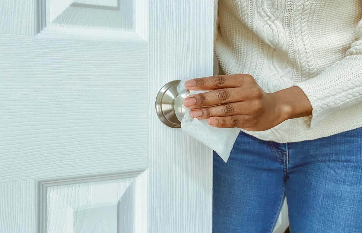 Woman Cleans Interior Doorknob Using Disinfectant Wipe