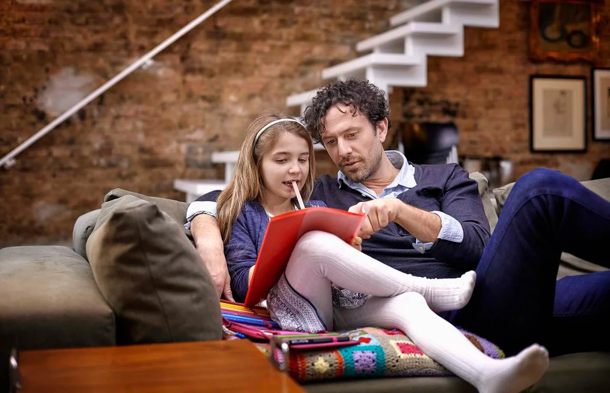 Father helping daughter with homework on couch