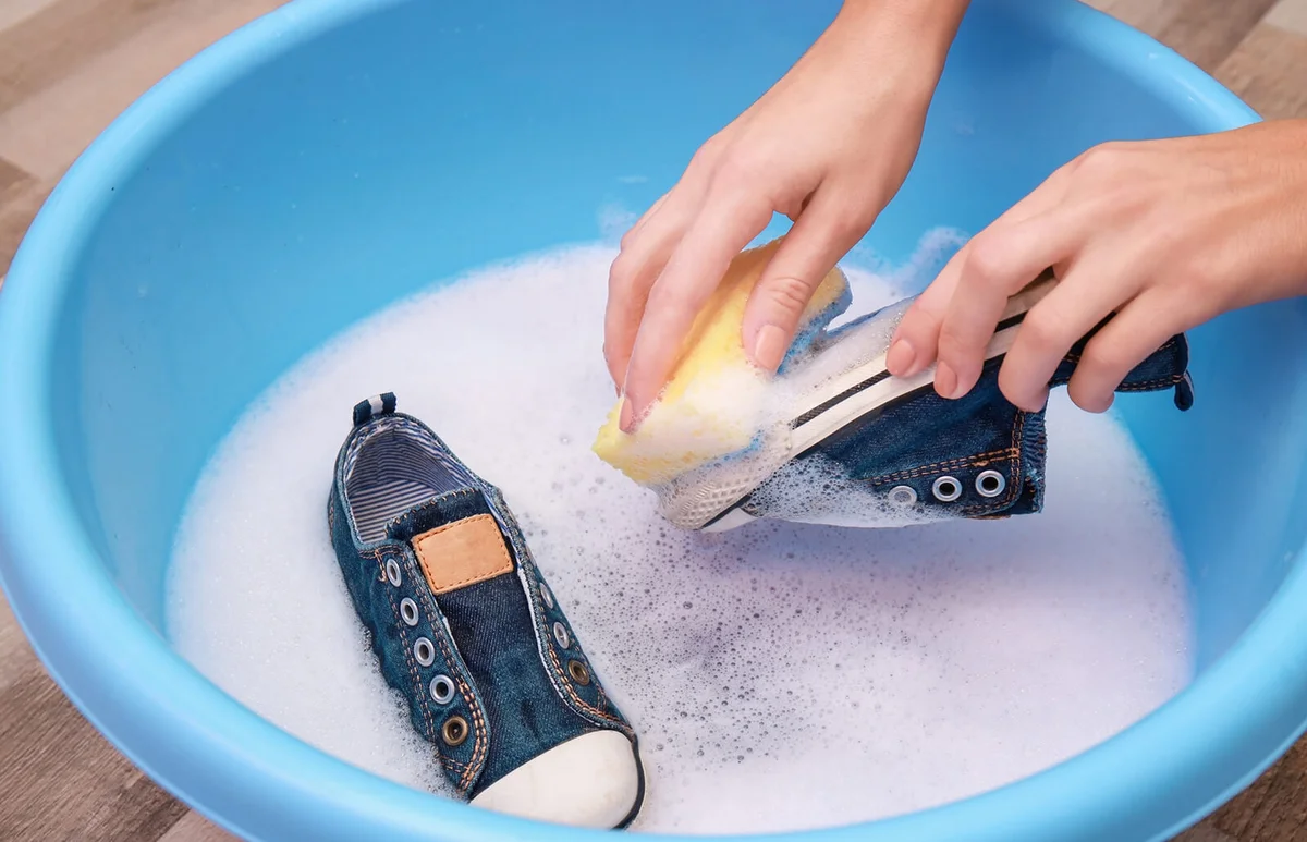 Woman washing sneakers with sponge over plastic basin