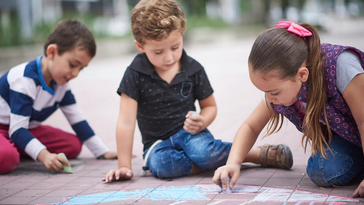 Hispanic boys and girl drawing with chalk on sidewalk