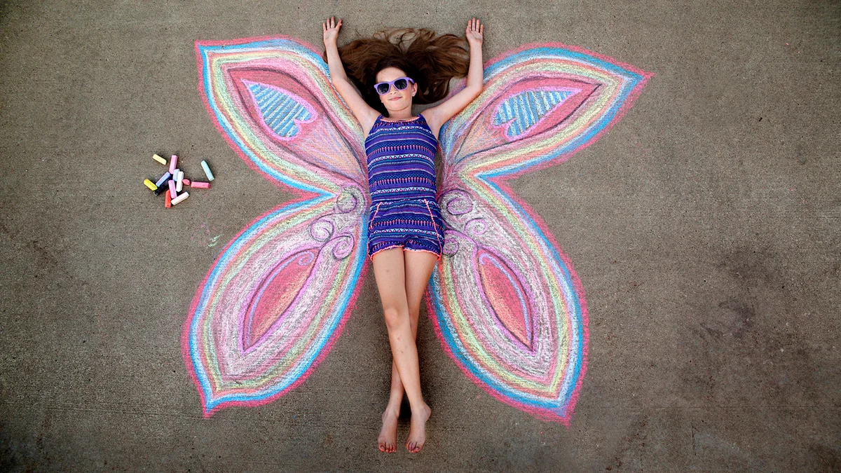 girl poses as the center of a butterfly drawn on the sidewalk with chalk