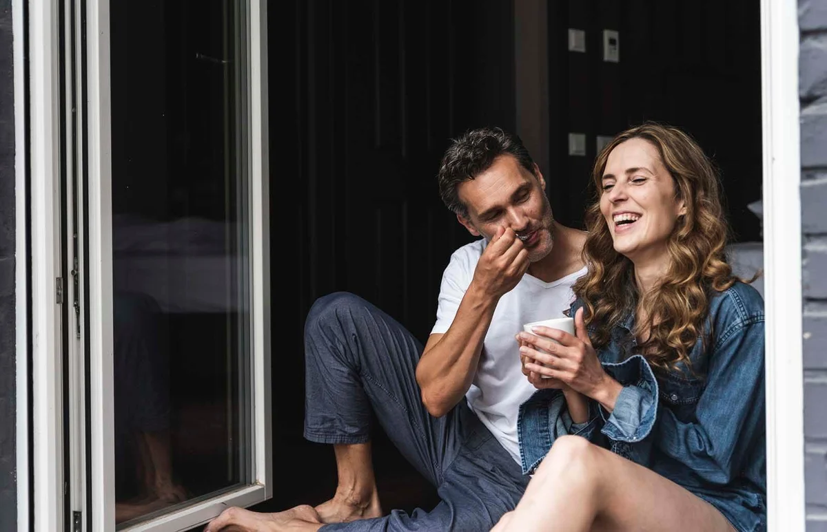Happy couple in nightwear at home sitting at French window