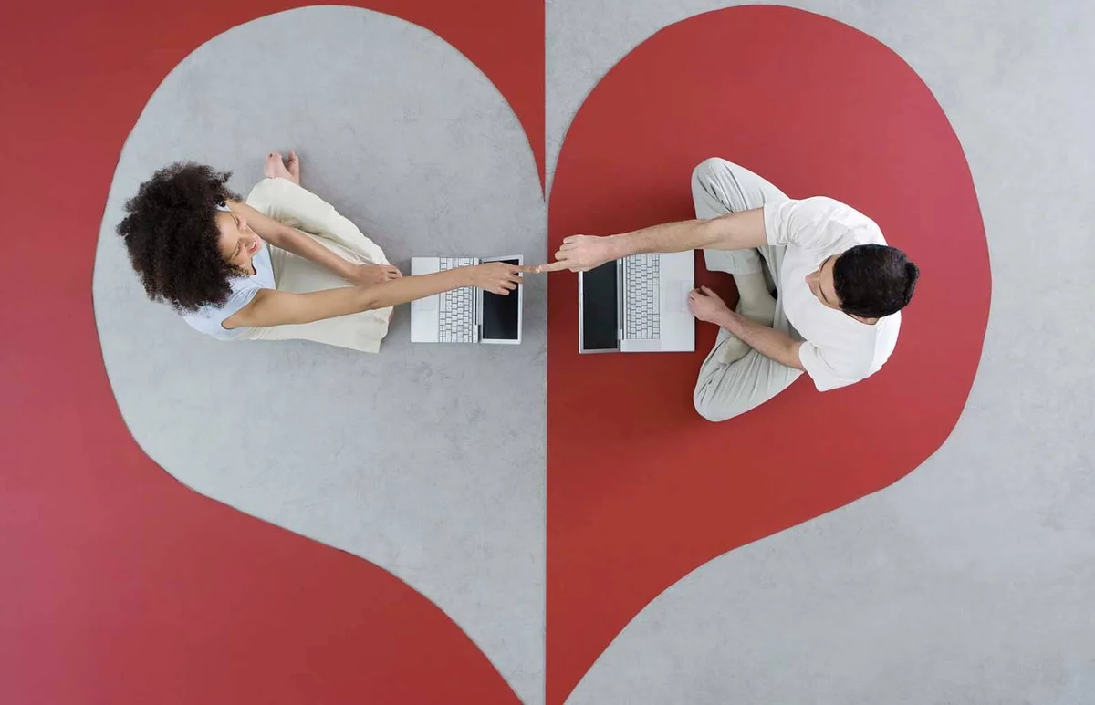 Couple sitting face to face with laptop computers on heart shape