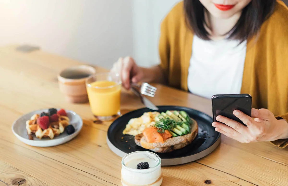 woman using smartphone while having breakfast