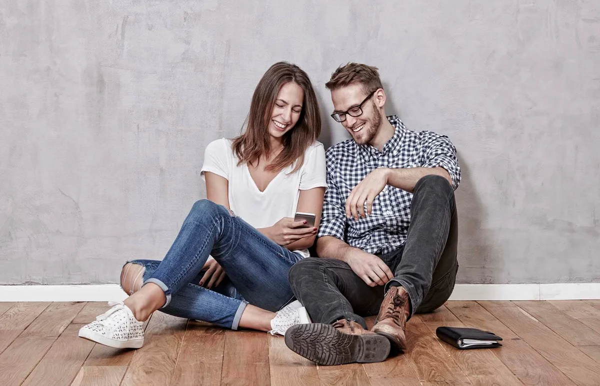 Smiling young couple sitting on the floor with cell phone