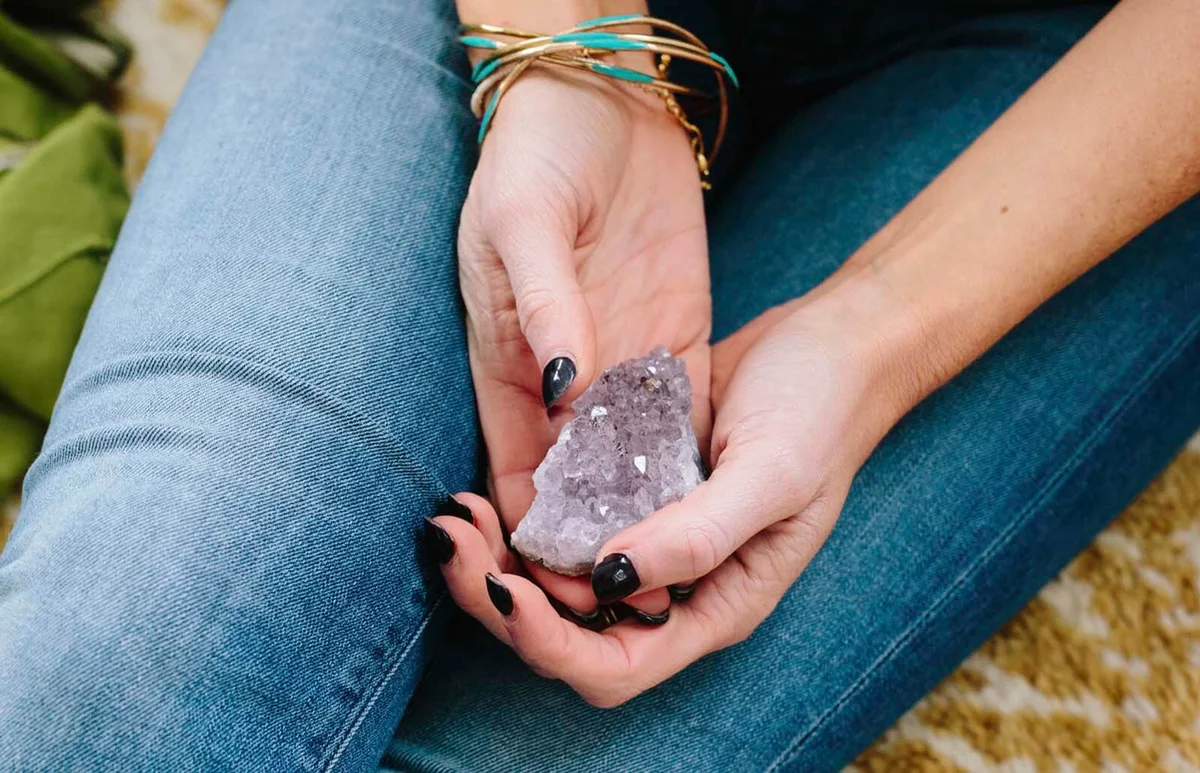 woman sitting holding a small purple crystal in her hands