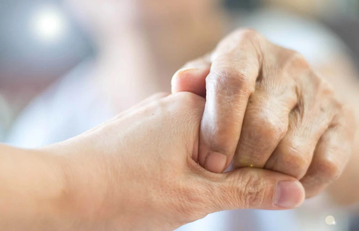 carer hand holding elder hand woman in hospice care